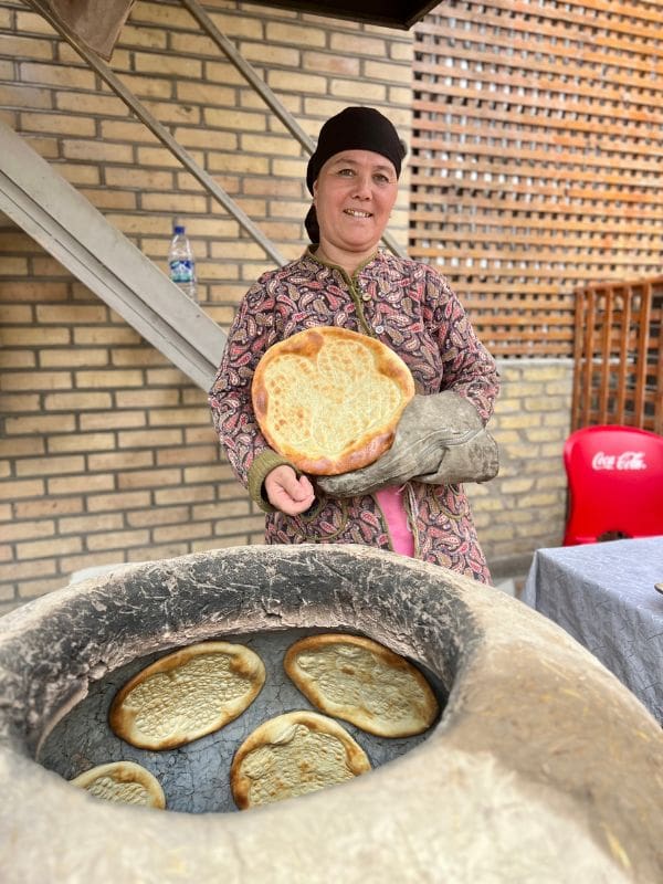 Uzbek lady holding bread standing near bread oven