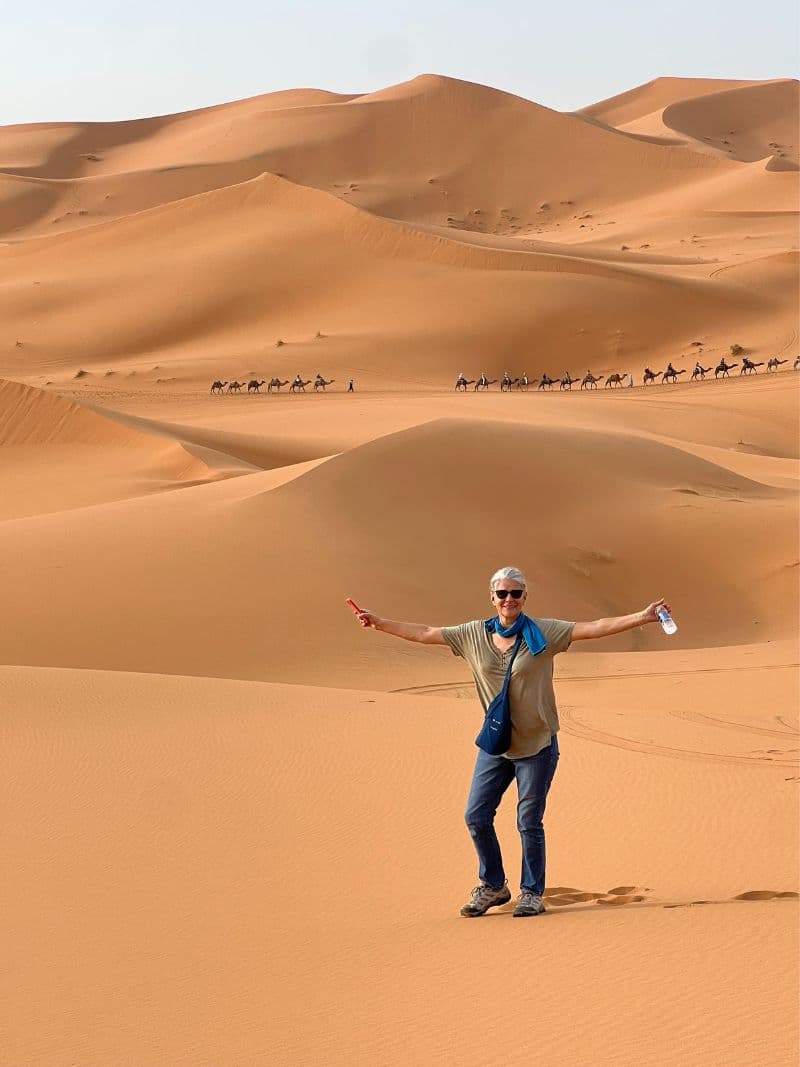 lady standing in Sahara with camel safari and sand dunes in background