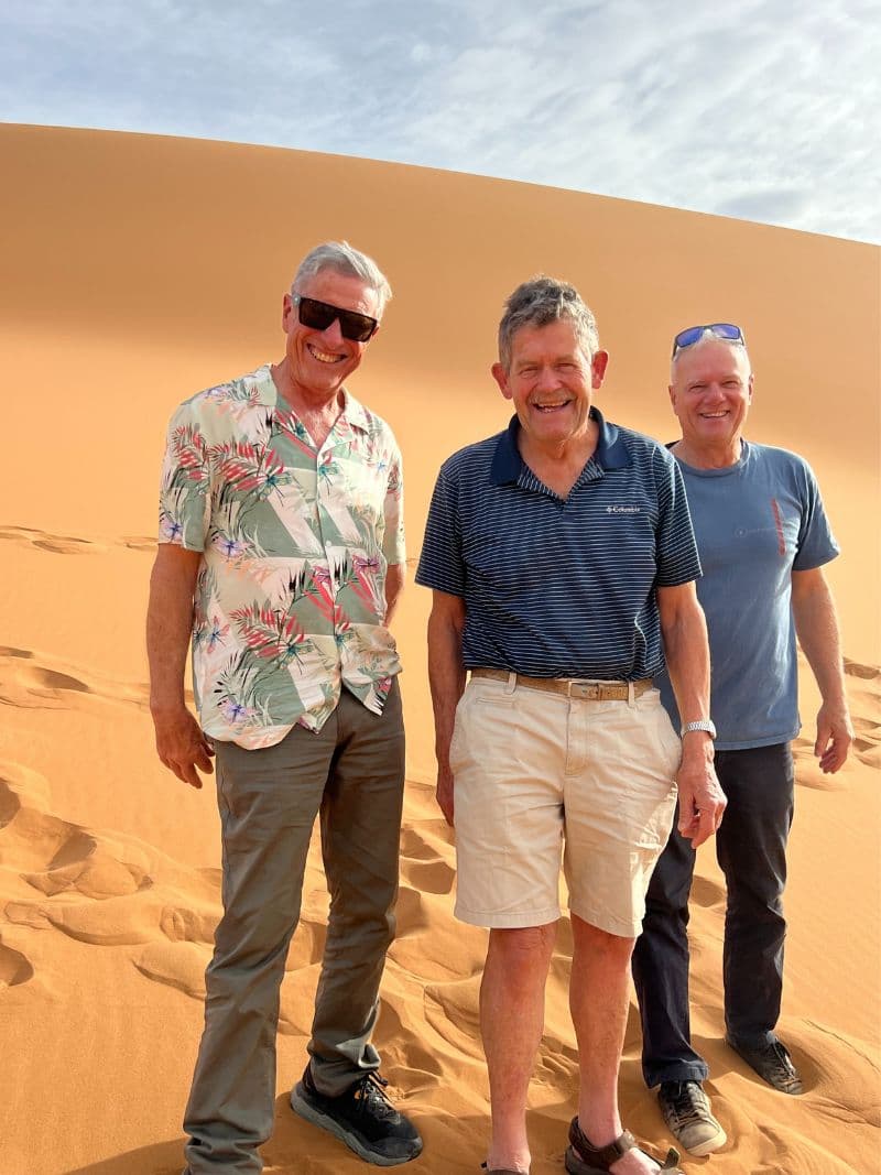 3 men standing in Sahara with sand dune in background